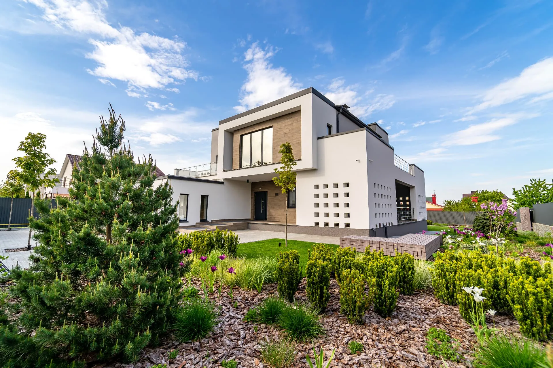A modern villa above a landscaped garden of pines, shrubs and flowering borders