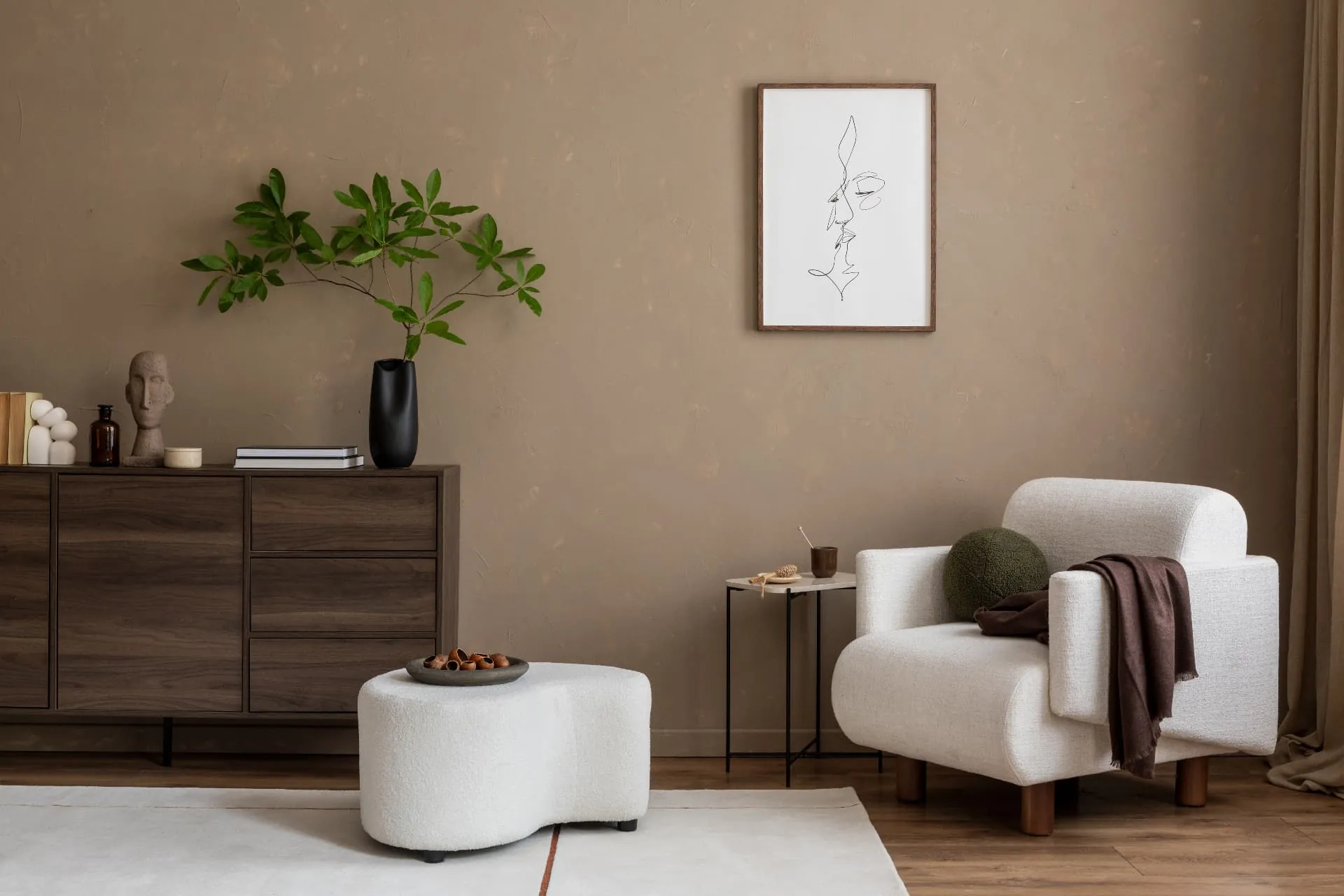 A warm plaster living room in taupe with a cream boucle armchair, walnut sideboard and a framed line drawing