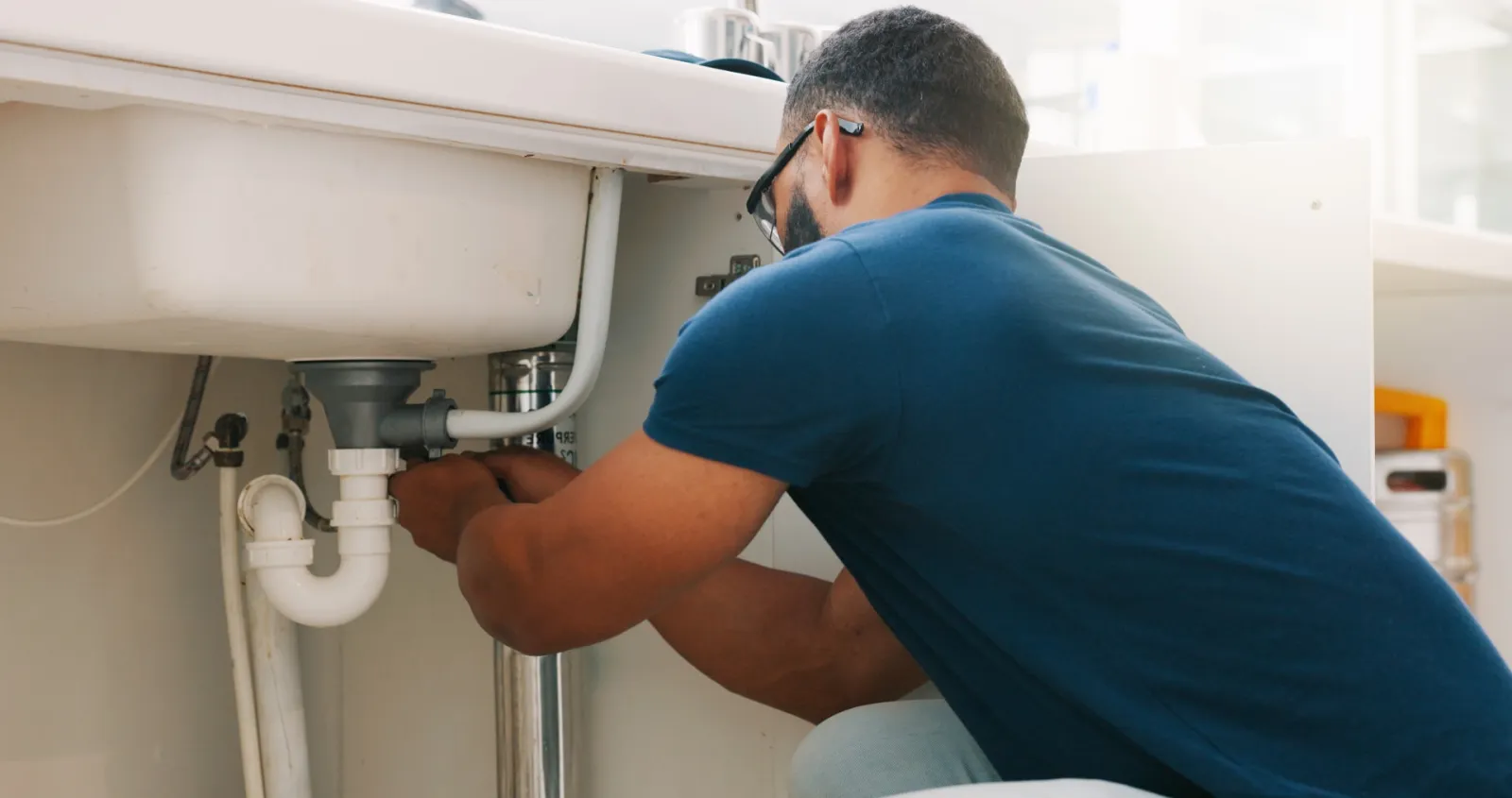 A plumber repairing pipework beneath a kitchen sink