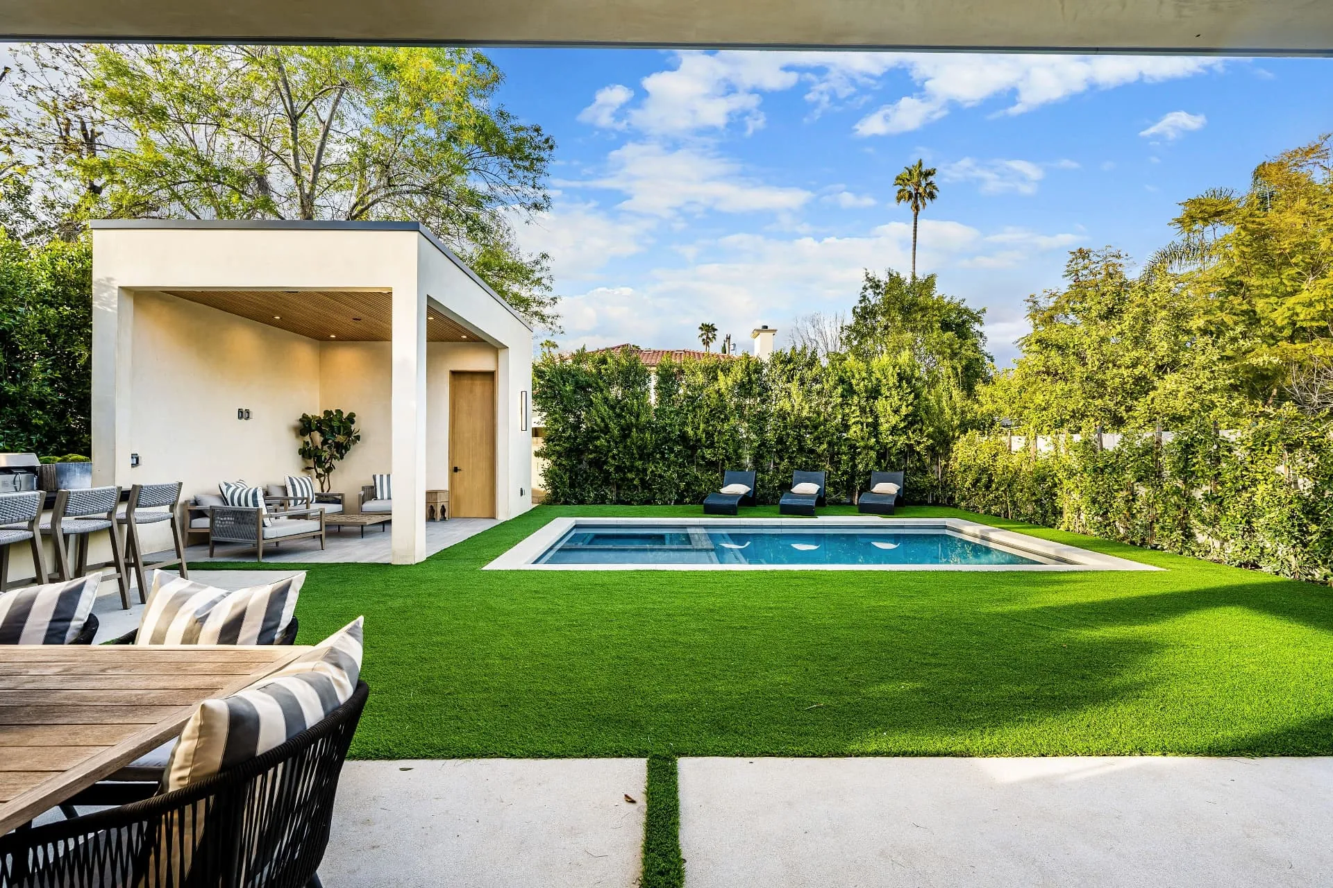 A lawn and pool garden framed by hedging, seen from a shaded terrace