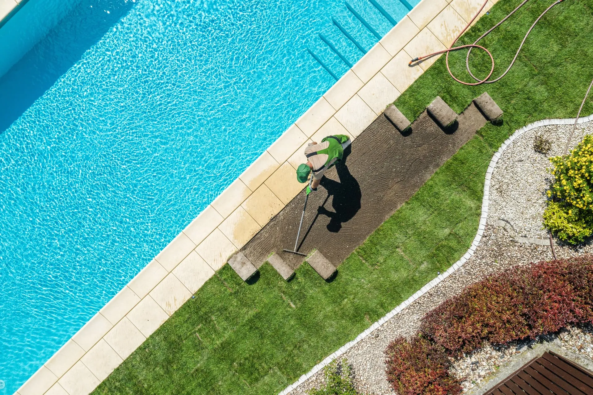 A gardener raking fresh gravel beside a swimming pool